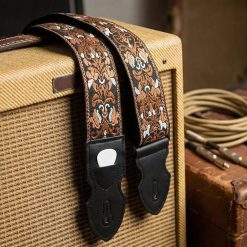 Sangle guitare vintage Baroque Bourbon à motif ornemental cuivré et blanc sur fond noir, posée sur un ampli vintage